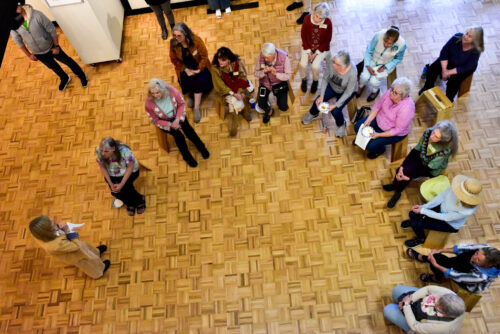 An aerial view of a group of people sitting down in a discussion. They are wearing casual clothes as they talk in the art studio.