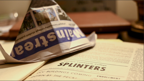  The current Newspaper "The Mainstream" is folded into a hat rests on top of the archive book. The page is opened to the "Splinters" , an old title of the newspaper